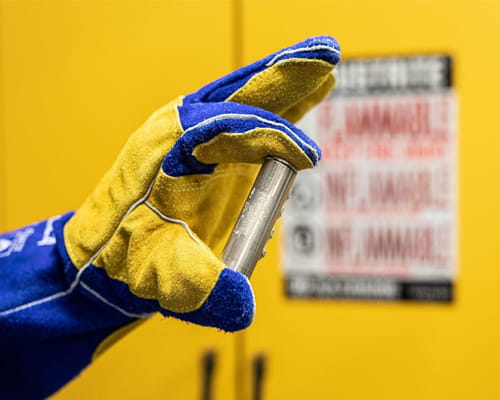 A gloved hand holding a metal cylinder object.