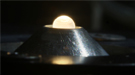 A metal oxide drop levitated in a flow of gas is being heated from above with a laser beam so that researchers can study the behavior of this class of ceramics under high temperatures.