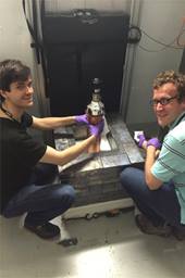 Bjorn Scholz (left) from the University of Chicago and Grayson Rich of the University of North Carolina at Chapel Hill and the Triangle Universities Nuclear Laboratory show off the world’s smallest neutrino detector, which is part of the COHERENT experiment.