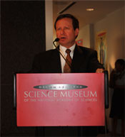 Dr. Koonin delivering a speech at a podium with a banner on the front reading Science Museum