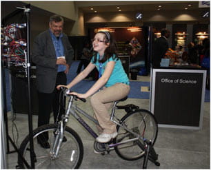 A young lady is trying out the stationary bike on display to see how much power she can generate