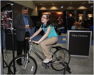 A young lady is trying out the stationary bike on display to see how much power she can generate