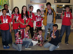 A group of students and their coach pose with their medals and trophies