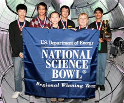 A group of students and their coach pose with their trophies and medals while holding a banner that reads US Dept of Energy National Science Bowl Regional Winning Team