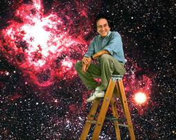 Scientist Saul Perlmutter sitting atop a ladder with a large image of the universe in the background