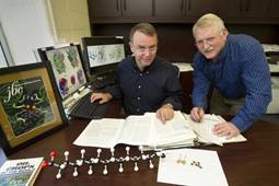 John Shanklin, biochemist at Brookhaven National Laboratory, and Ed Whittle, research assistant in Shanklin's lab, with a fatty acid molecule model and plant seeds and casings in the foreground.