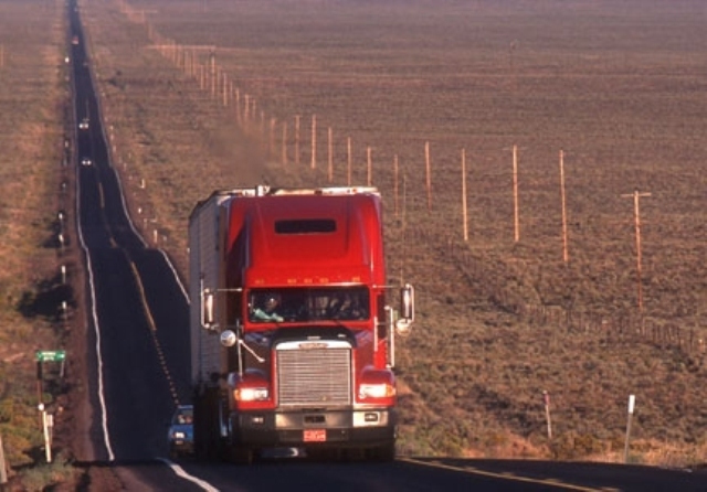 Tractor trailer driving down road flanked by fields