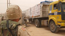 A US soldier in the foreground looking over a large cargo truck carrying cases of water