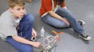 A boy sitting on the floor with a helicopter and bottle of glue