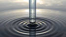 A tunnel of water flowing into a placid body of water with a symmetrical ripple effect thumbnail.