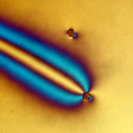 Silica microparticle on a yellow background showing a light yellow light and two arched blue lights coming from the particle.