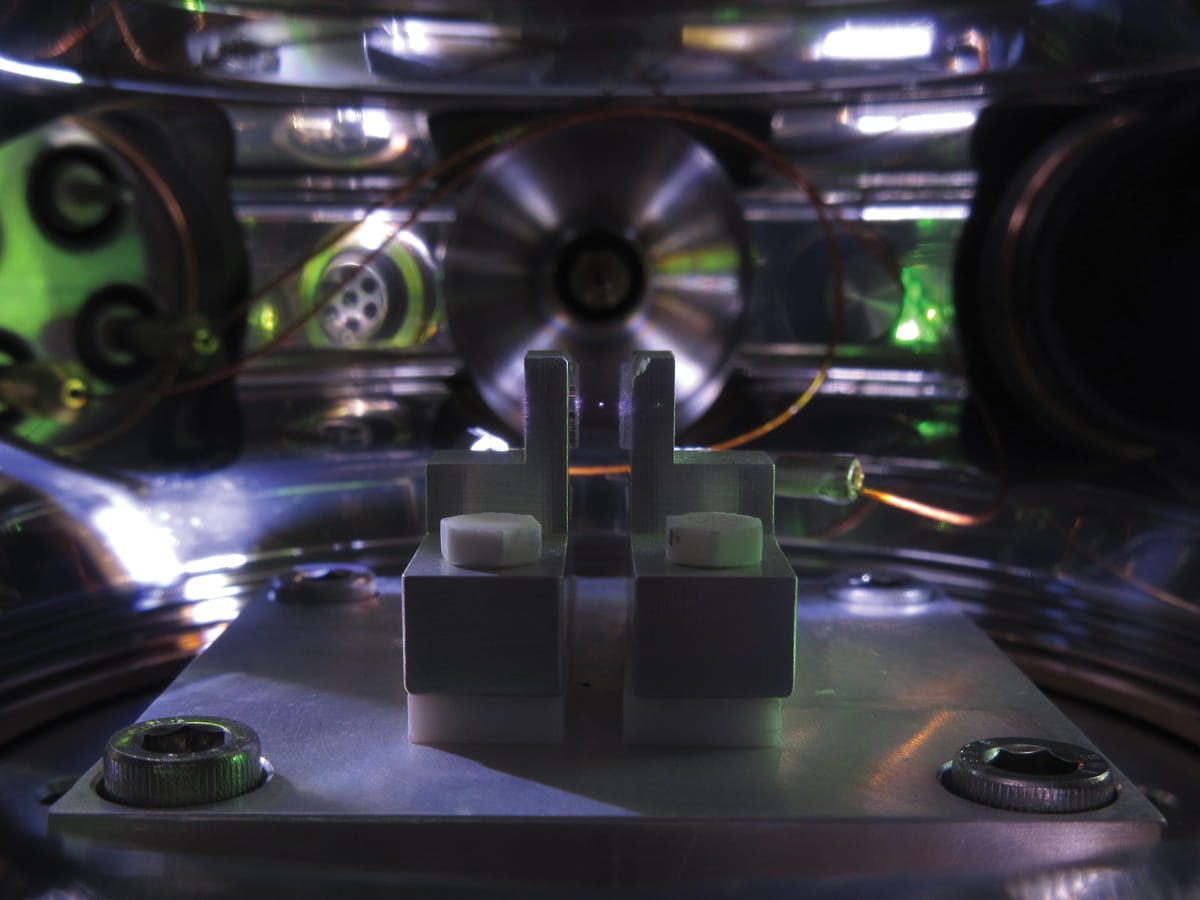Photograph of an optically trapped microparticle in high vacuum. The microparticle is visible as a white dot levitated between two lenses, which are used to focus and collect the invisible infrared laser light used to trap the particle. 